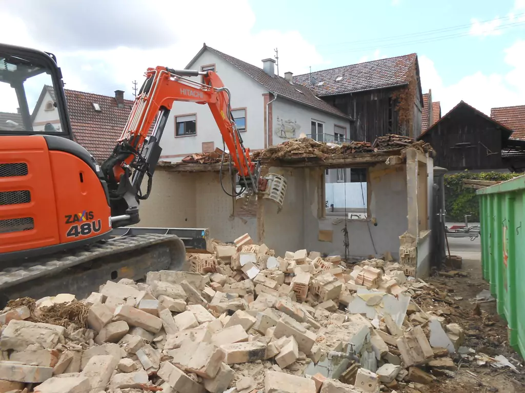 roter Bagger bei Abbrucharbeiten einer Hauswand auf einer Baustelle