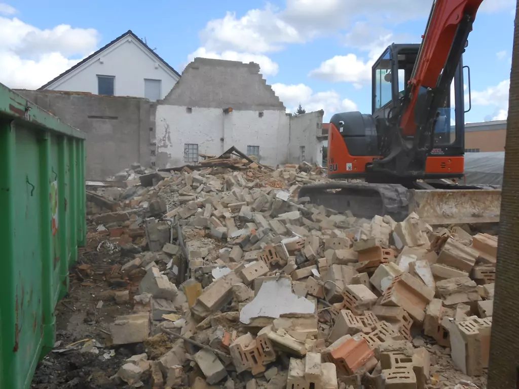 Frontansicht eines roten Baggers bei Abbrucharbeiten auf einer Baustelle