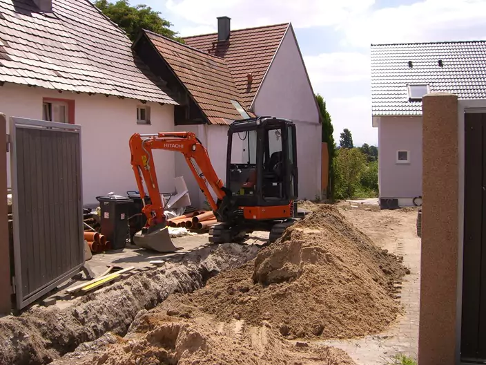 kleiner roter Bagger auf einer Baustelle bei Kanalaushebungsarbeiten